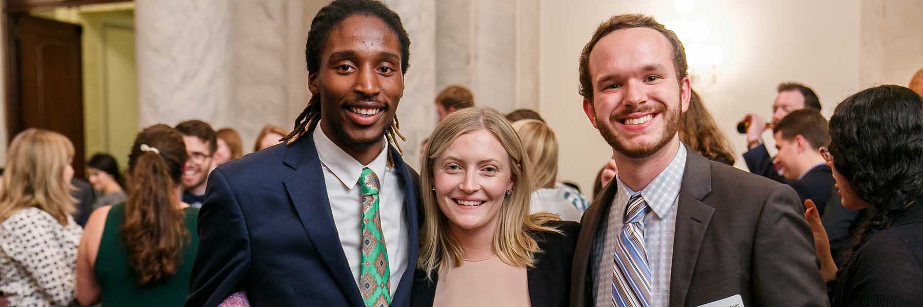 Three smiling students in a marble pillared government building event. 